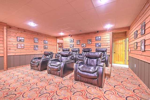 carpeted cinema room featuring a paneled ceiling and wood walls