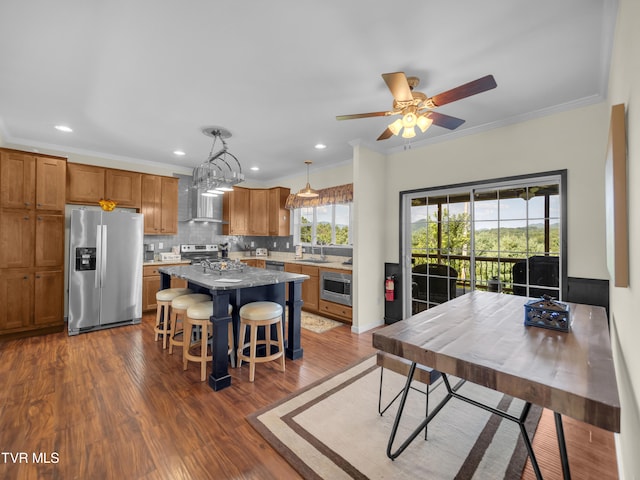 kitchen with pendant lighting, ceiling fan with notable chandelier, stainless steel appliances, dark hardwood / wood-style flooring, and a center island