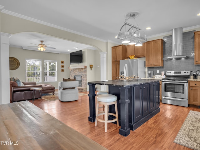 kitchen featuring a kitchen island, a breakfast bar, stainless steel appliances, wall chimney range hood, and light wood-type flooring