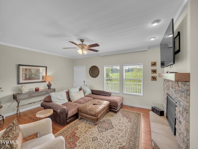 living room featuring light wood-type flooring, ornamental molding, ceiling fan, and a stone fireplace