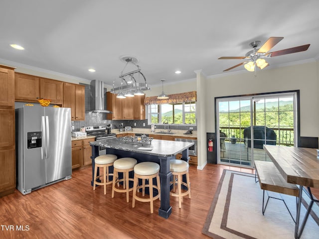 kitchen featuring wall chimney exhaust hood, appliances with stainless steel finishes, hardwood / wood-style flooring, and a center island