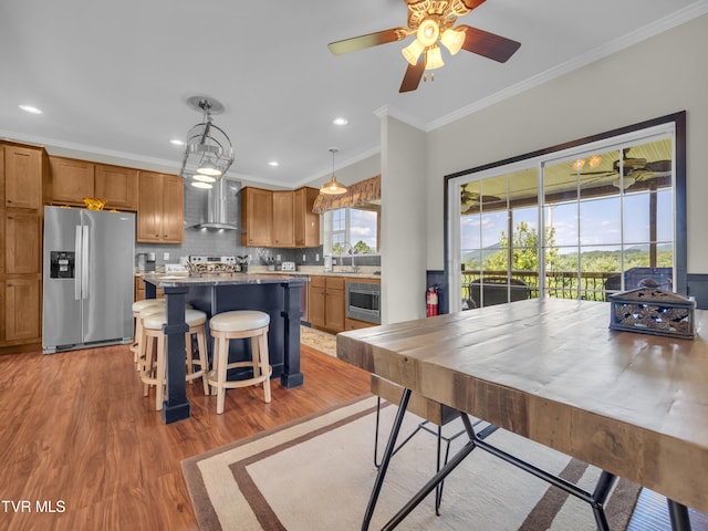 kitchen featuring hanging light fixtures, a center island, appliances with stainless steel finishes, wall chimney range hood, and ceiling fan