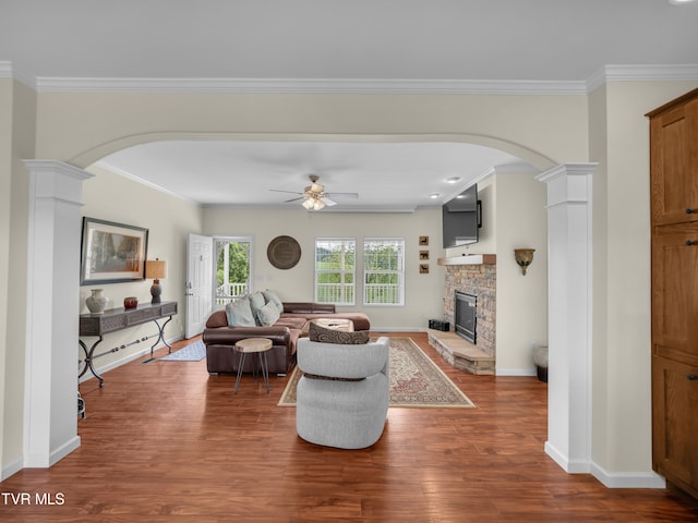 living room with dark hardwood / wood-style flooring, a fireplace, decorative columns, ornamental molding, and ceiling fan