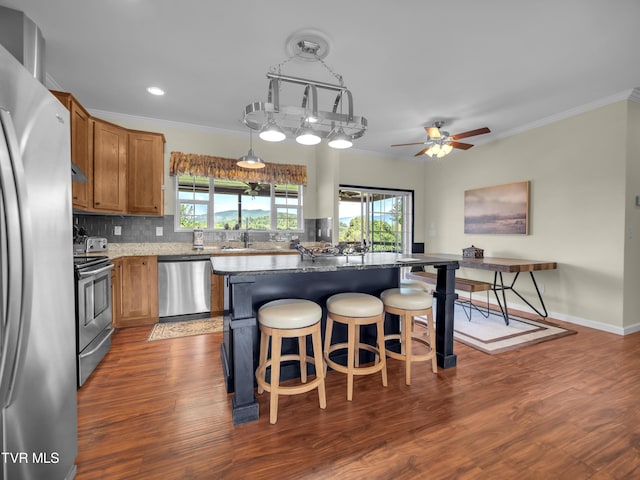 kitchen with a kitchen breakfast bar, dark hardwood / wood-style floors, ceiling fan with notable chandelier, appliances with stainless steel finishes, and a center island