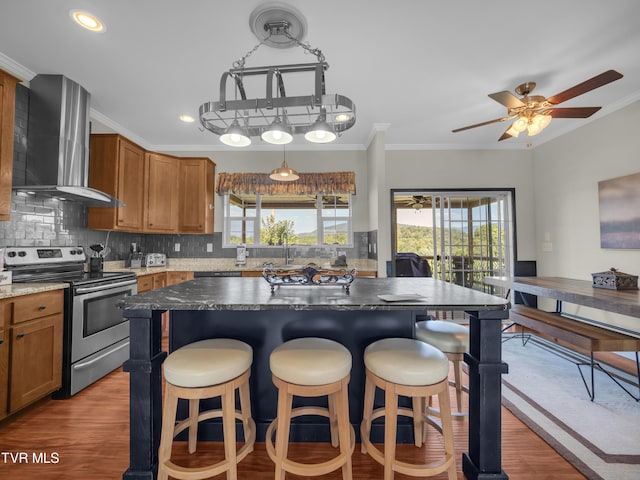 kitchen featuring a healthy amount of sunlight, ceiling fan, stainless steel electric range oven, and wall chimney range hood