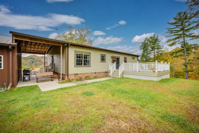 rear view of house with a wooden deck, a lawn, and a patio