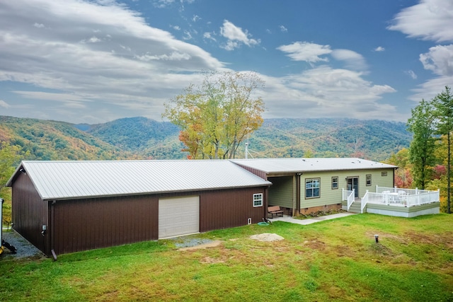 rear view of property with an outdoor structure, a yard, a deck with mountain view, and a garage