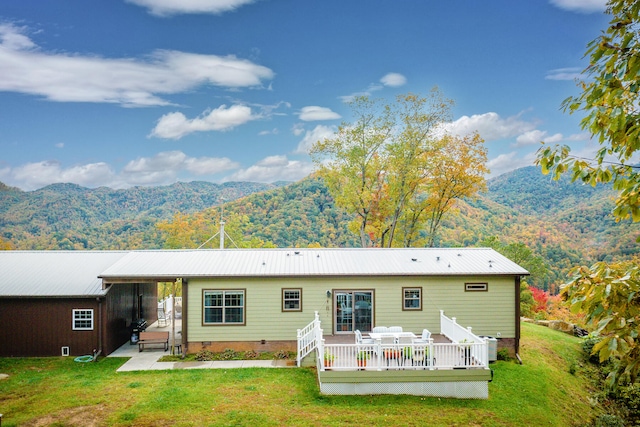 rear view of property with a deck with mountain view and a yard