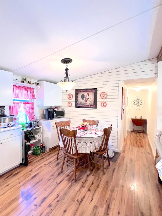 dining room featuring light hardwood / wood-style floors, lofted ceiling, and wood walls