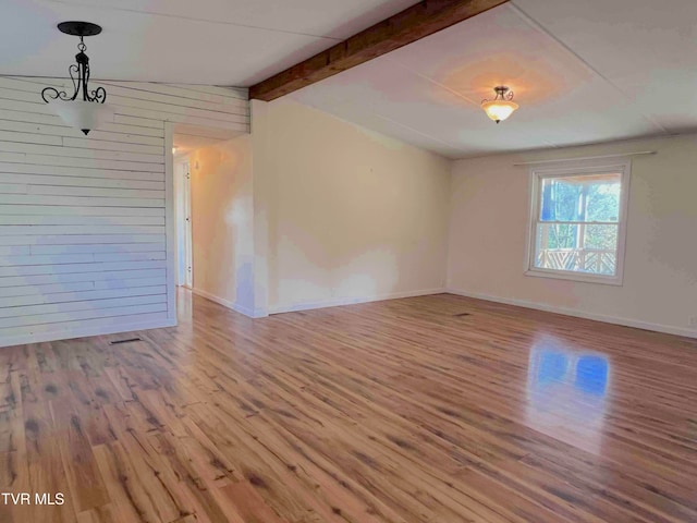 spare room featuring vaulted ceiling with beams, wooden walls, and light hardwood / wood-style flooring