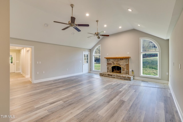 unfurnished living room featuring a fireplace, ceiling fan, a wealth of natural light, and light hardwood / wood-style flooring