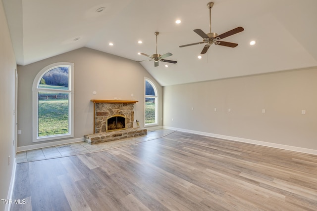 unfurnished living room with lofted ceiling, a stone fireplace, ceiling fan, and light hardwood / wood-style flooring