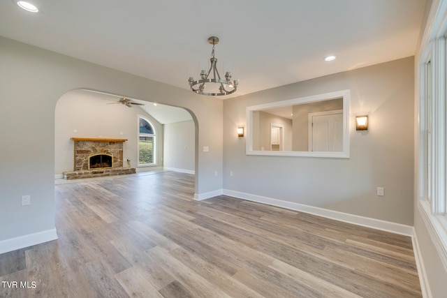 unfurnished living room featuring a stone fireplace, ceiling fan with notable chandelier, and light hardwood / wood-style flooring