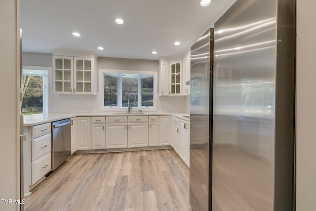 kitchen featuring sink, backsplash, light hardwood / wood-style floors, stainless steel appliances, and white cabinetry