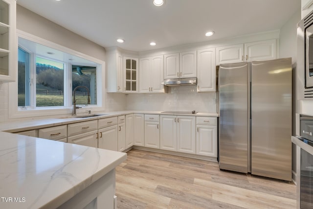 kitchen with stainless steel fridge, white cabinets, light hardwood / wood-style flooring, and light stone counters