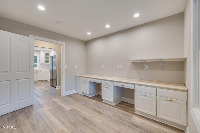 unfurnished office featuring built in desk and light hardwood / wood-style floors