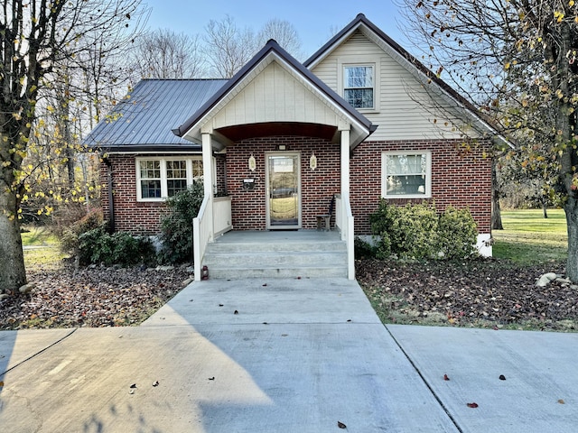 bungalow-style house with brick siding, a porch, metal roof, and a standing seam roof