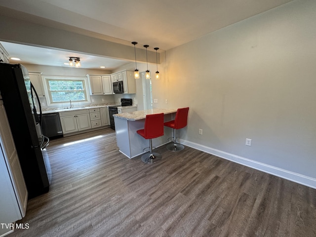 kitchen featuring black appliances, a breakfast bar, a sink, dark wood finished floors, and baseboards