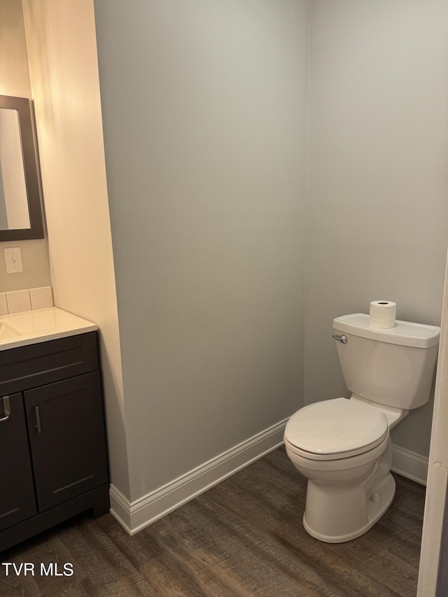 half bathroom with toilet, vanity, baseboards, and wood finished floors