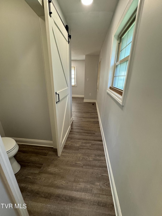 hall featuring a barn door, baseboards, and dark wood-style floors