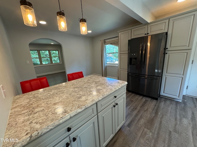 kitchen with light stone countertops, stainless steel fridge, dark hardwood / wood-style flooring, a healthy amount of sunlight, and pendant lighting