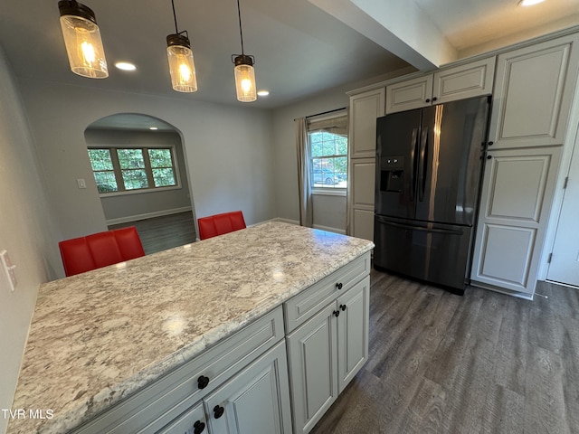 kitchen featuring dark wood-type flooring, baseboards, hanging light fixtures, black fridge, and arched walkways