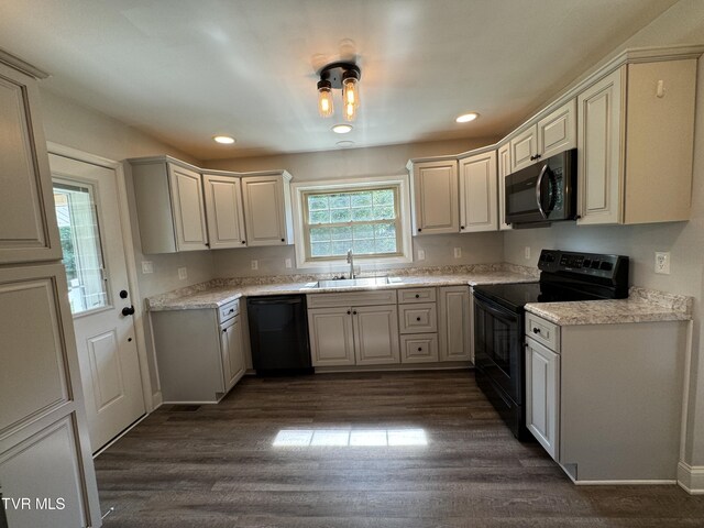 kitchen featuring dark wood-type flooring, light stone counters, sink, and black appliances