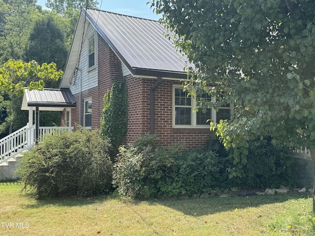 view of side of property featuring brick siding, metal roof, and a yard