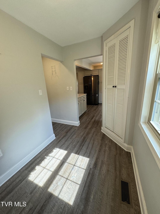 unfurnished bedroom with visible vents, baseboards, dark wood-style flooring, black fridge with ice dispenser, and a closet