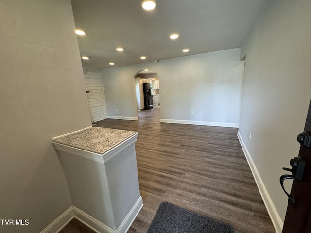 empty room featuring recessed lighting, baseboards, arched walkways, and dark wood-type flooring