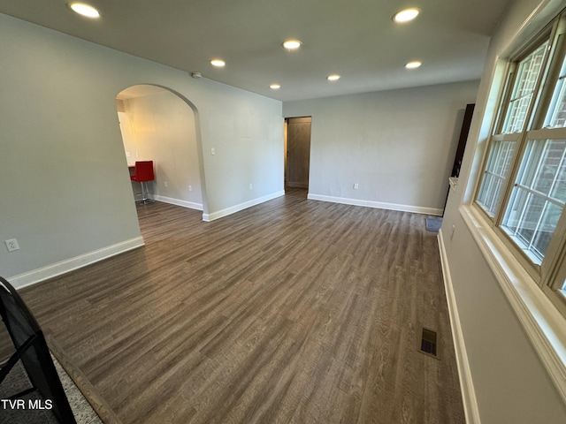 spare room featuring visible vents, baseboards, recessed lighting, arched walkways, and dark wood-type flooring