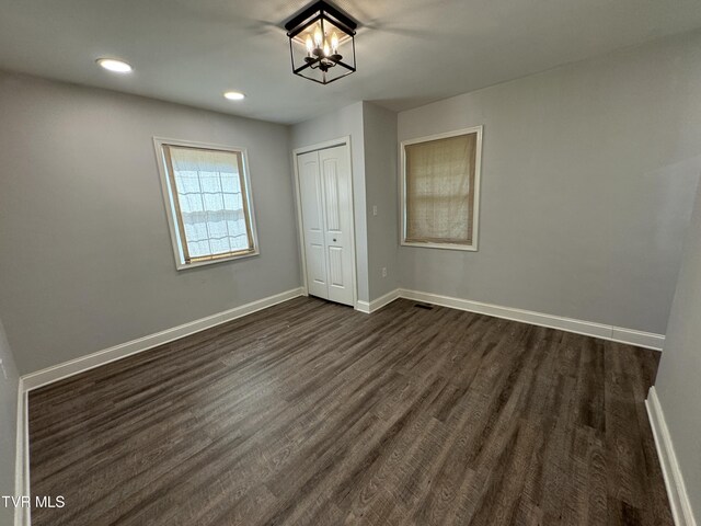 unfurnished bedroom with a chandelier, a closet, and dark wood-type flooring