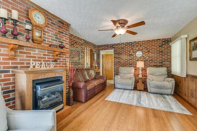 living room with ceiling fan, brick wall, light hardwood / wood-style floors, and a textured ceiling