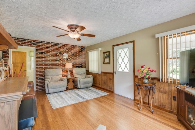 living room with ceiling fan, brick wall, a textured ceiling, and light hardwood / wood-style floors