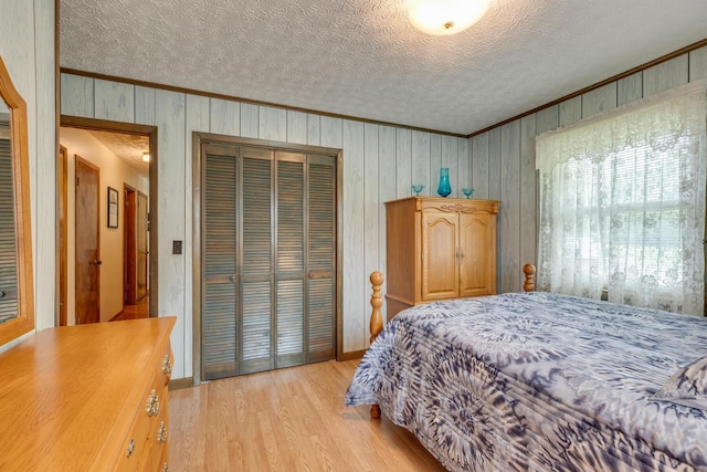 bedroom featuring light wood-type flooring, a textured ceiling, wooden walls, and a closet