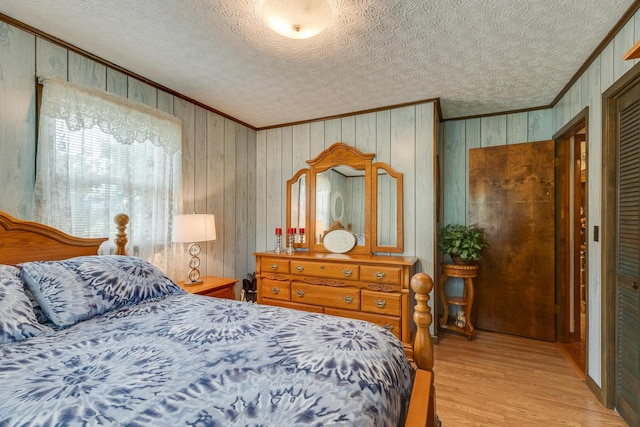 bedroom featuring wood walls, light hardwood / wood-style floors, a textured ceiling, and ornamental molding