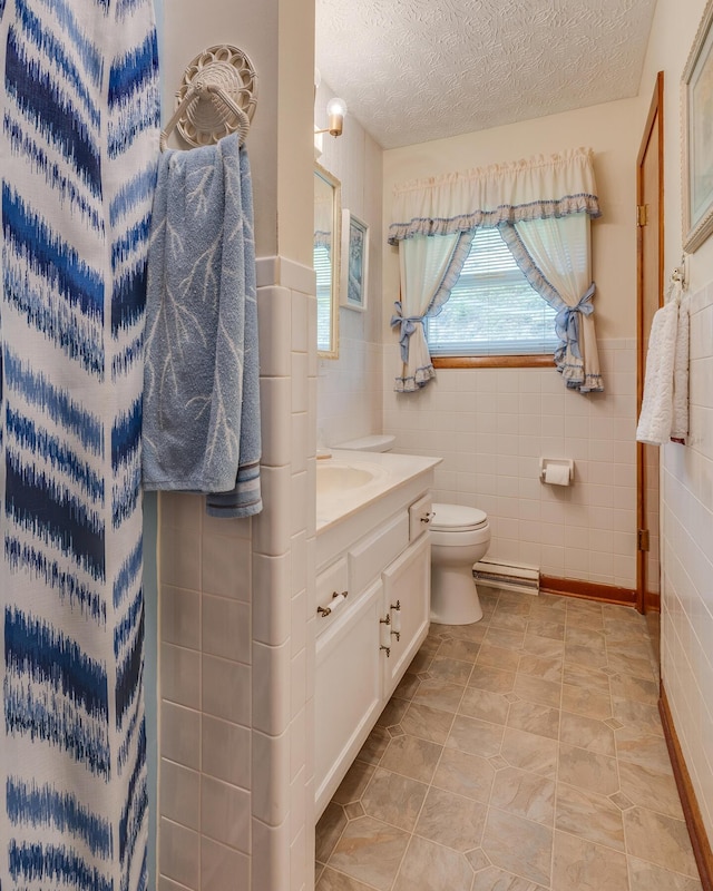 bathroom with vanity, toilet, a textured ceiling, baseboard heating, and tile walls