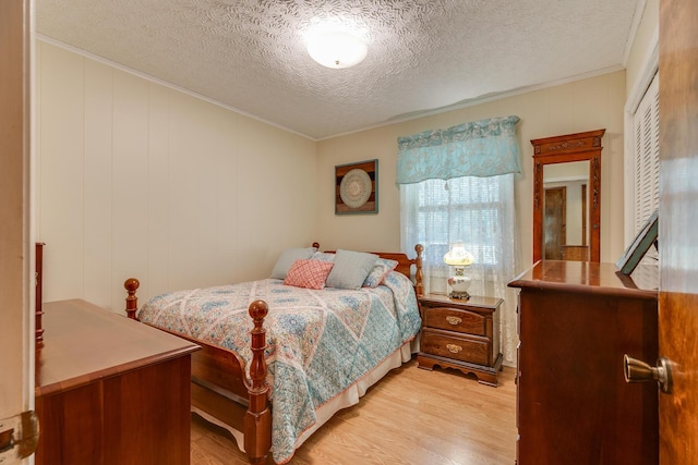 bedroom with light hardwood / wood-style floors, a textured ceiling, and ornamental molding