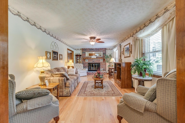 living room featuring ceiling fan, a fireplace, light hardwood / wood-style floors, and a textured ceiling