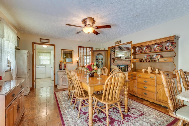 dining space featuring washer and clothes dryer, ceiling fan, a fireplace, and a textured ceiling