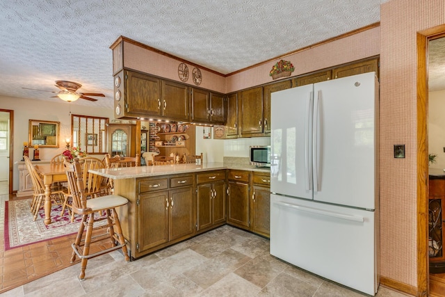 kitchen with kitchen peninsula, ceiling fan, crown molding, white fridge, and a breakfast bar area