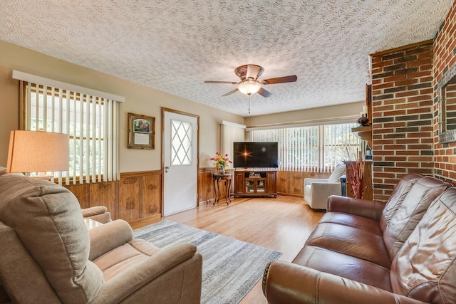 living room with ceiling fan, wood walls, light hardwood / wood-style floors, and a textured ceiling