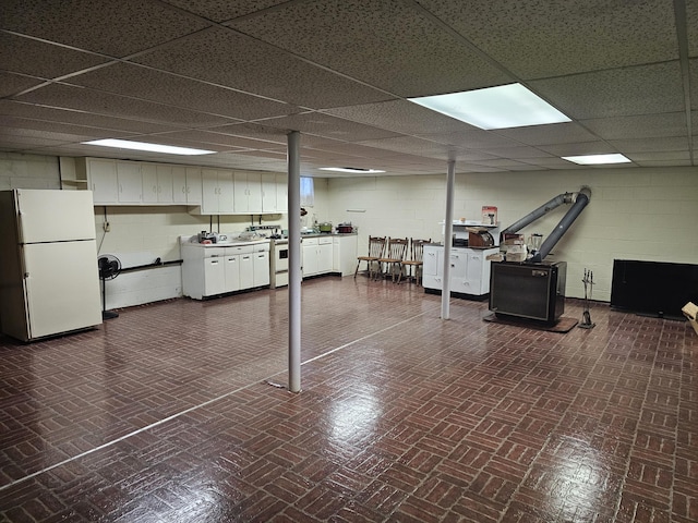 basement with a paneled ceiling and white fridge