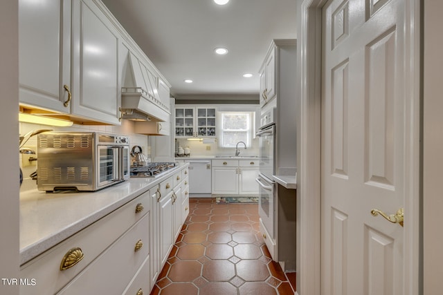 kitchen with dark tile floors, white cabinetry, stainless steel appliances, premium range hood, and sink