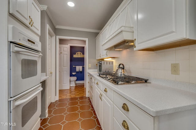 kitchen with dark parquet floors, tasteful backsplash, premium range hood, double oven, and white cabinetry