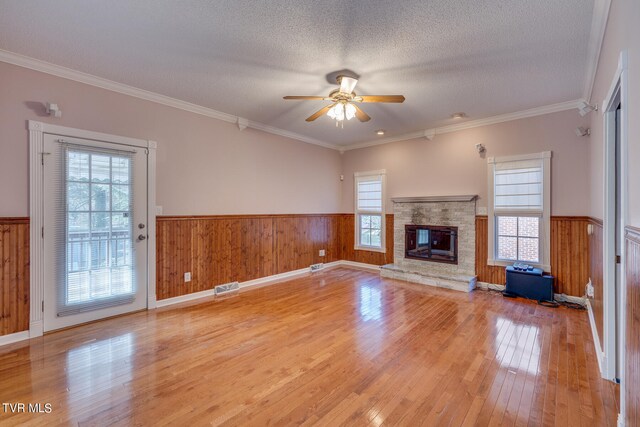 unfurnished living room with light wood-type flooring, crown molding, a stone fireplace, and a healthy amount of sunlight