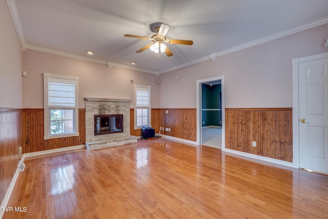 unfurnished living room with light hardwood / wood-style flooring, ornamental molding, a textured ceiling, ceiling fan, and a stone fireplace