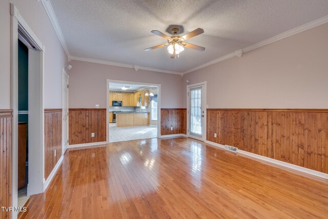 empty room with light hardwood / wood-style floors, ornamental molding, and a textured ceiling