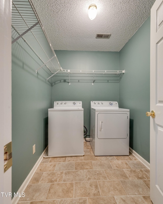 clothes washing area with a textured ceiling, separate washer and dryer, and light tile patterned floors