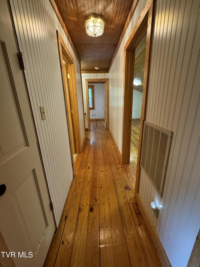 hallway featuring light wood-type flooring, wooden walls, and wooden ceiling